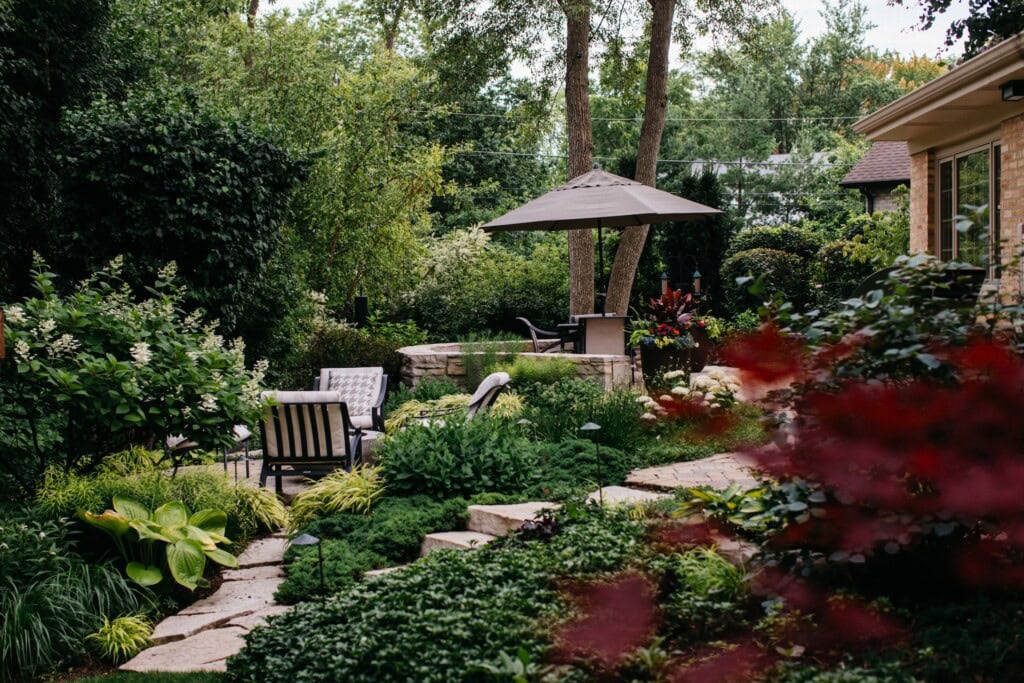A multi-tiered backyard paver and natural stone patio surrounded by lush landscaping in Northbrook, IL | Milieu Landscaping